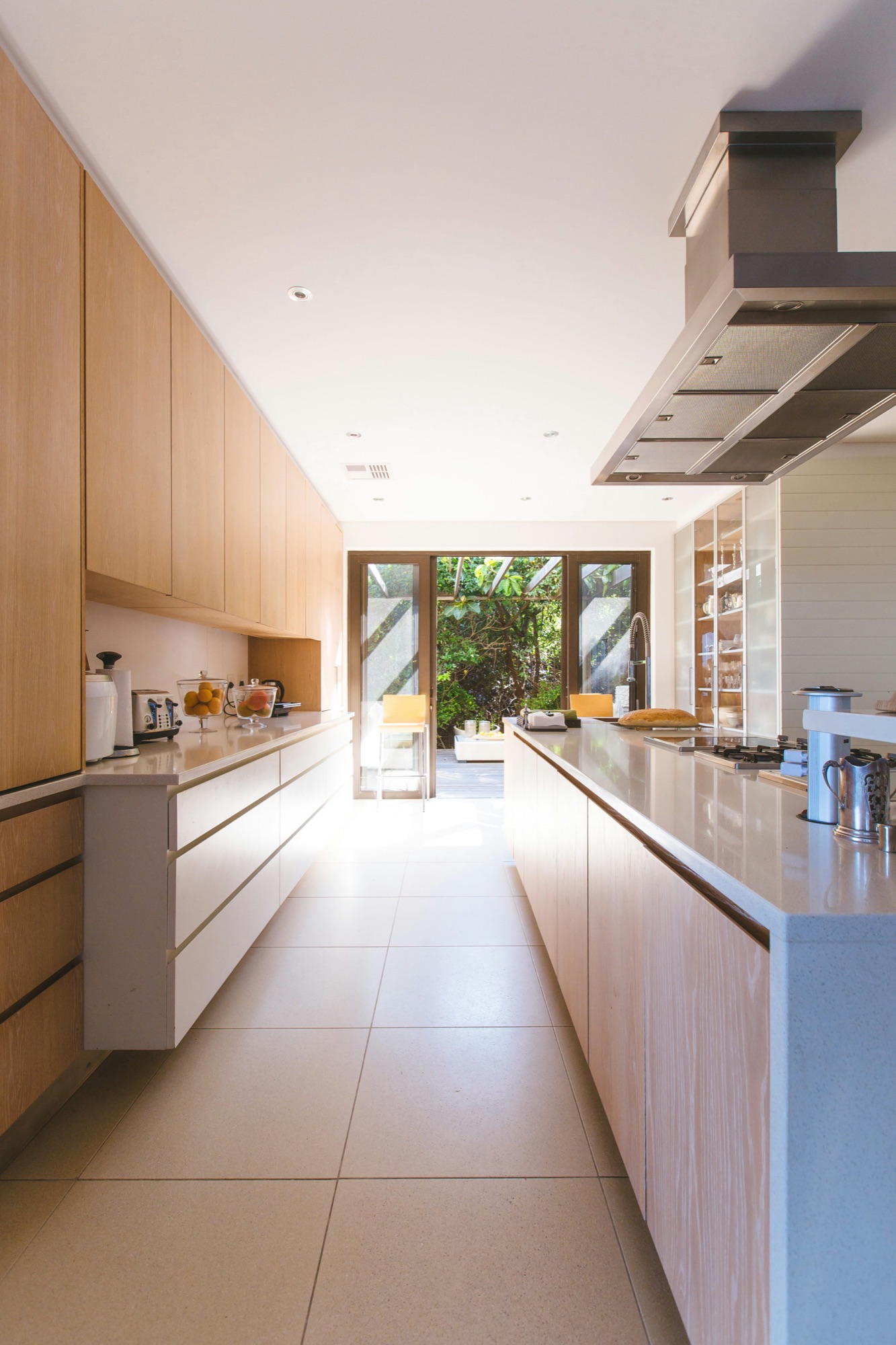 Sunlit galley kitchen with polished countertops opening onto a garden